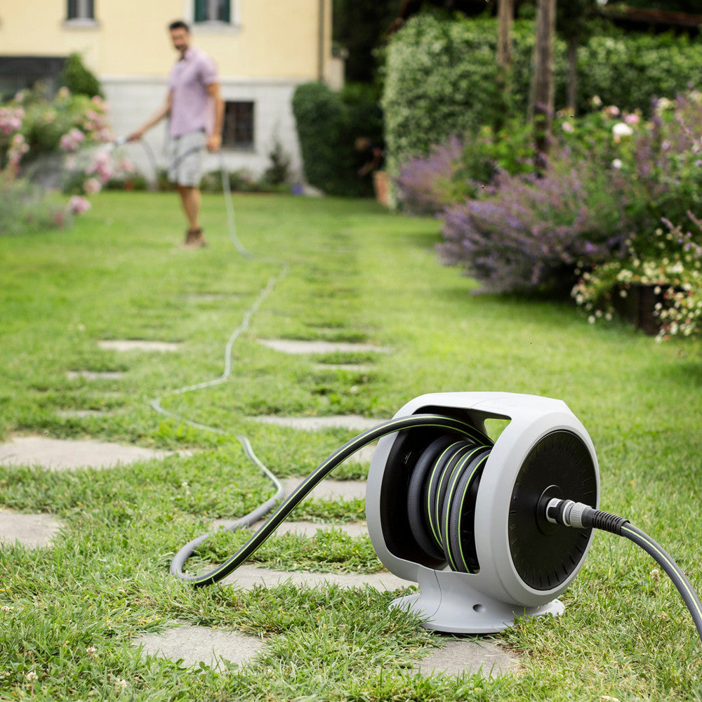 FITT hose reel featuring a compact design, suitable for extensive gardens and irrigation activities, showcased in a grassy area with a user in the background, HOSE FITT With Reel - Made In Italy (5 YEARS WARRANTY).